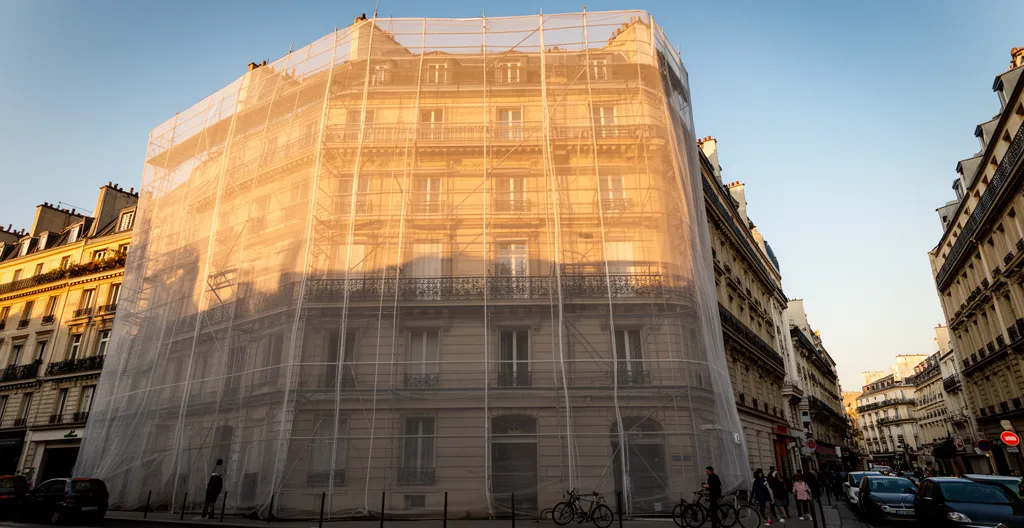 Façade d'immeuble haussmannien avec échafaudage et bâche publicitaire pendant des travaux de ravalement