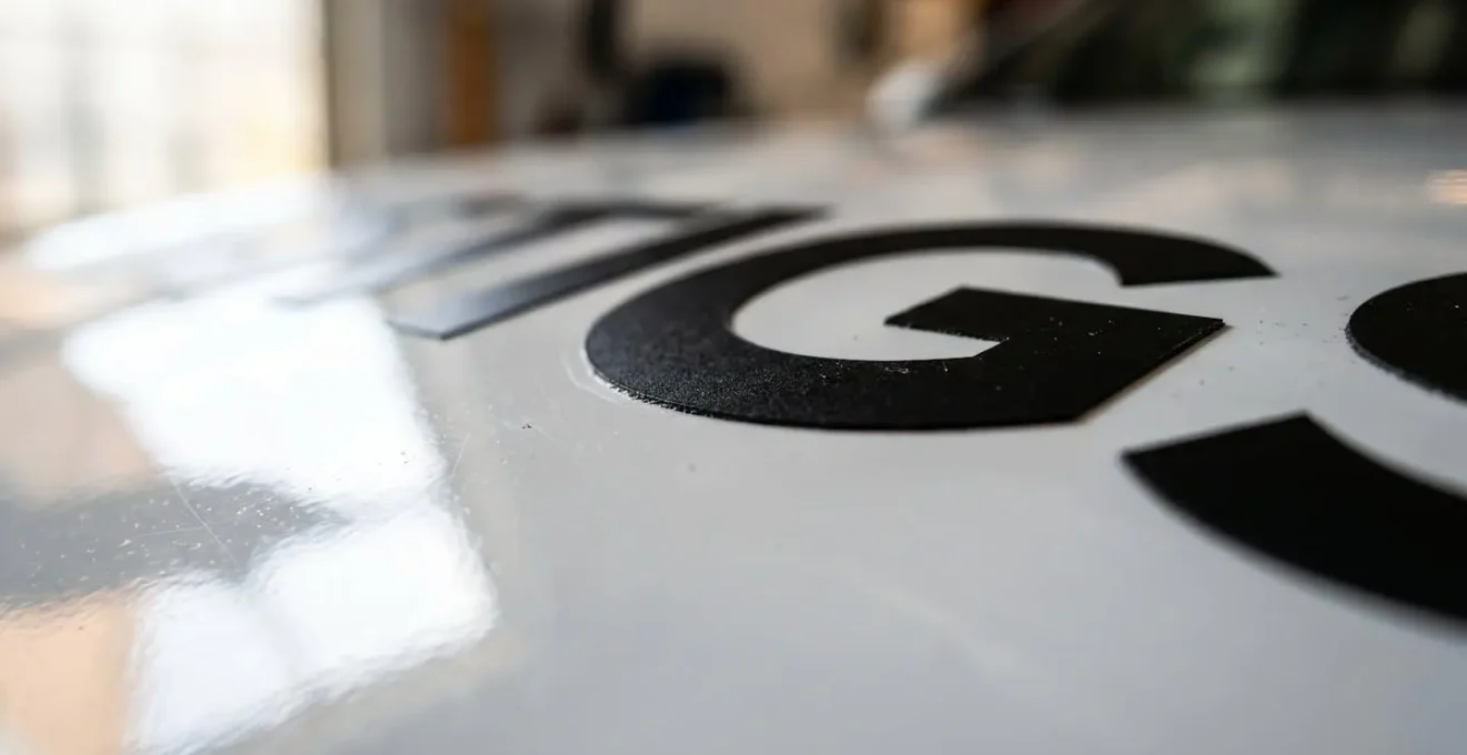 Détail macro d'un lettrage adhésif découpé sur carrosserie blanche créant un jeu de contraste graphique